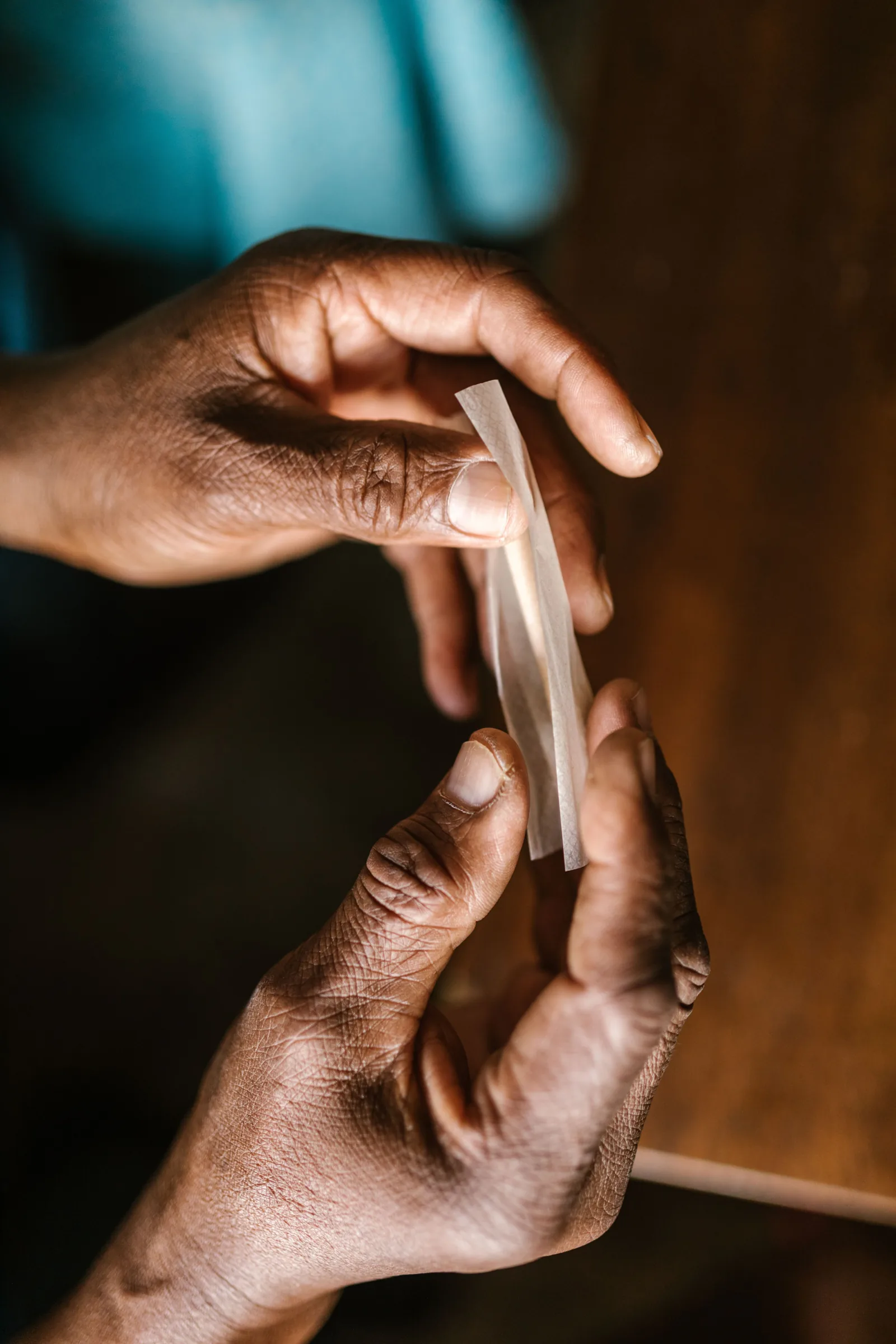 Close-up of hands working with rolling paper at a wooden table.
