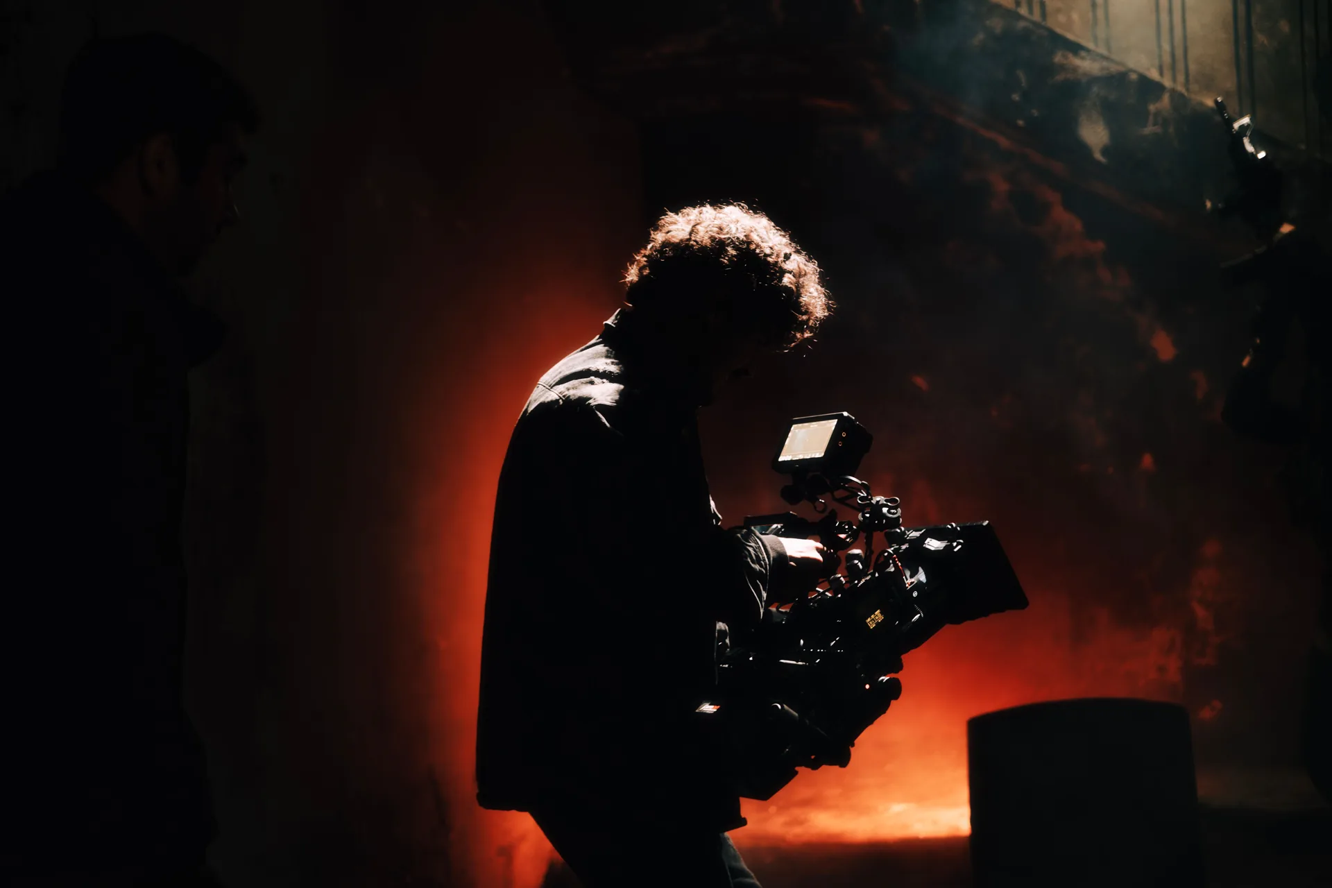 A camera operator silhouetted against red light on a film set.